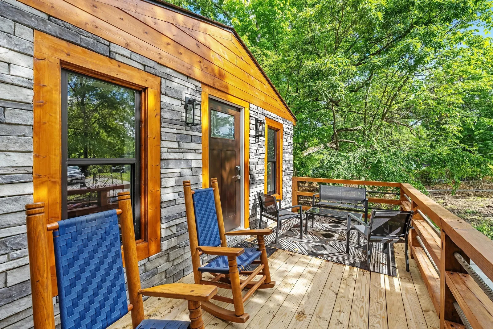 A renovated tiny house with cedar trim, stone siding and two rocking chairs on the porch